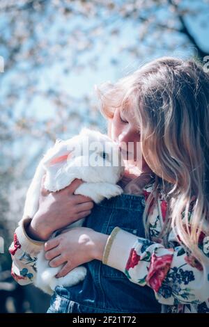 Liebenswert schöne Mädchen mit langen blonden Haaren umarmt weißen Ostern Kaninchentier Stockfoto