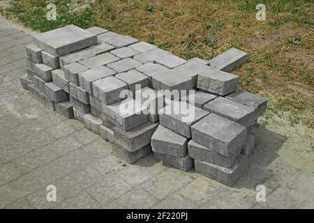 Stapel von grauen Pflasterplatten auf der Seite von gestapelt Straße in der Nähe einer verlassenen Rasen vor der Reparatur der Bürgersteig Stockfoto