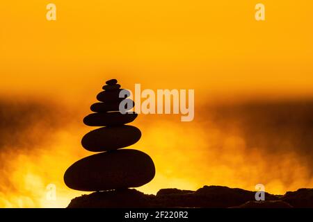Ausgewogene Kieselsteinpyramide Silhouette am Strand. Abstrakt warmen Sonnenuntergang Bokeh mit Meer auf dem Hintergrund. Zen-Steine am Meer Strand, Meditation, Spa Stockfoto