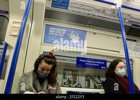 Passagiere und covid 19 Pandemie Gesicht Abdeckung und soziale Distanzierung Schilder auf die londoner U-Bahn-Züge 2021 Stockfoto