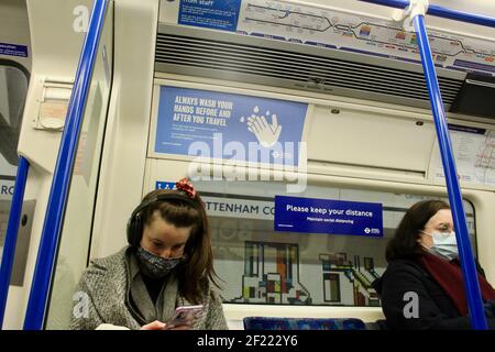 Passagiere und covid 19 Pandemie Gesicht Abdeckung und soziale Distanzierung Schilder auf die londoner U-Bahn-Züge 2021 Stockfoto