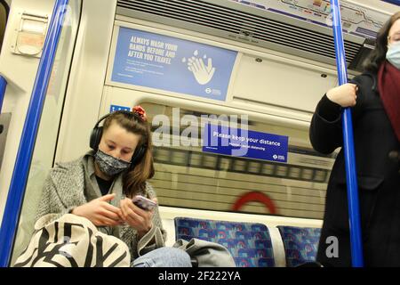 Passagiere und covid 19 Pandemie Gesicht Abdeckung und soziale Distanzierung Schilder auf die londoner U-Bahn-Züge 2021 Stockfoto