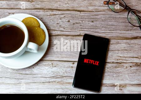 Ein Handy oder Handy auf einem Holz gelegt Tisch mit der Netflix App Öffnung auch einen Kaffee und Brille Stockfoto
