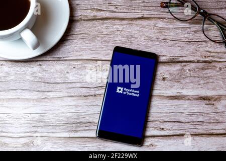 Ein Handy oder Handy auf einem Holz gelegt Tabelle mit der Royal Bank of Scotland App als nächstes öffnen Zu einem Kaffee Stockfoto