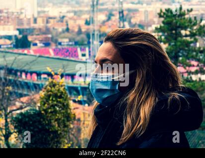 Frau mit Maske auf Gesicht Profilansicht besorgt über Coronavirus Pandemie mit Blick auf eine Stadt und Stadion in der Hintergrund Stockfoto