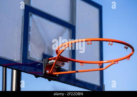 Ein Porträt eines Outdoor-Basketball-Felge ohne Netz und ein Plexiglas-Backboard mit blauen Linien auf ihm vor einem blauen Himmel. Der Basketballkorb oder Stockfoto