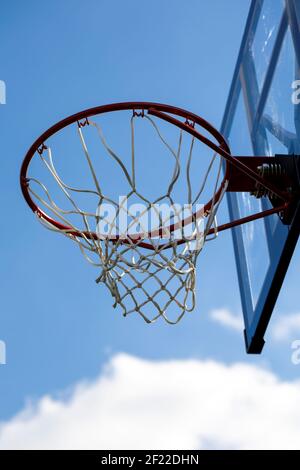 Ein Porträt eines Outdoor-Basketball-Felge mit einem Netz und einem Plexiglas-Backboard mit blauen Linien auf ihm vor einem blauen Himmel. Der Basketballkorb oder der Rin Stockfoto