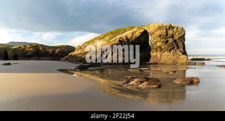 Ein warmer goldener Morgen an einem Sandstrand mit zackigen Und schroffen Klippen Stockfoto