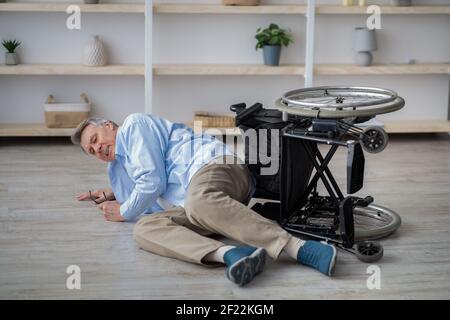 Behinderter älterer Mann, der auf dem Boden lag, nachdem sein Rollstuhl gestürzte Drinnen Stockfoto