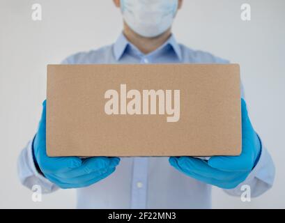 Delivery Mann hält Kartons in medizinischen Handschuhen und Schutzmaske auf weißem Hintergrund. Die Versandzeit Coronavirus. Stockfoto