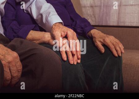 Ein älteres Paar, das sich gegenseitig auf dem Sofa stützt. Der alte Mann hält die Hand der Frau im Pflegeheim. Liebe zum Tod. Die Hände sehr alter Menschen. Stockfoto