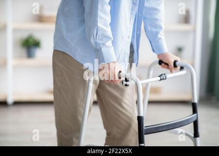 Beschnittene Ansicht eines älteren Mannes, der zu Hause mit Rahmen läuft, Nahaufnahme. Behinderte ältere Person, die professionelle Hilfe benötigt Stockfoto