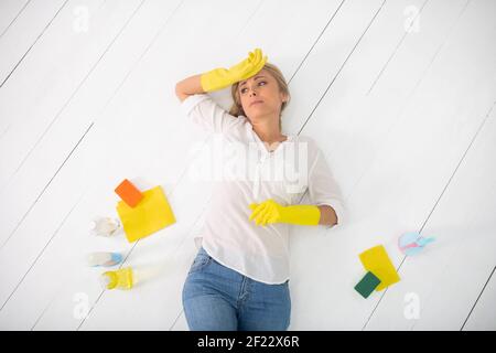 Müde Hausfrau in gelben Handschuhen auf dem Boden liegen Stockfoto