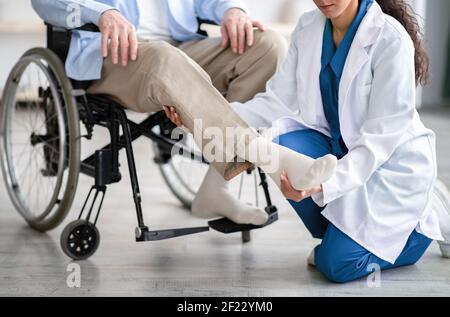 Beschnittene Ansicht eines jungen Arztes, der das Bein eines behinderten älteren Patienten untersucht Während eines Arztbesuches zu Hause Stockfoto