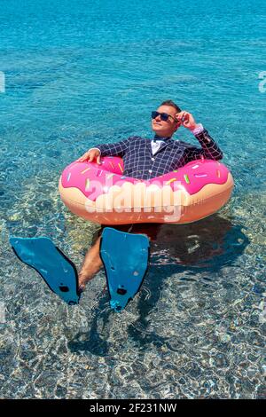 Glücklicher Geschäftsmann in Flossen auf einem aufblasbaren Donut im Meer. Sommerurlaub Konzept. Stockfoto