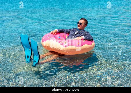 Glücklicher Geschäftsmann in Flossen auf einem aufblasbaren Donut im Meer. Sommerurlaub Konzept. Stockfoto