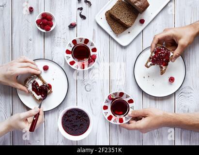 Mann und Frau trinken Tee und essen Toast mit Himbeere Gelee beim Frühstück auf weißem Holztisch Stockfoto
