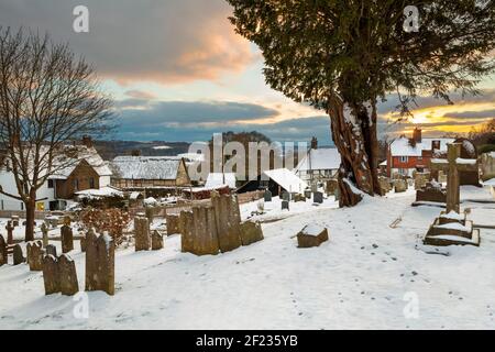 Schneebedeckter Kirchhof der St. Bartholomew Kirche mit Hütten hinter bei Sonnenuntergang, Burwash, East Sussex, England, Vereinigtes Königreich, Europa Stockfoto