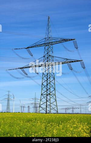 Ein Strommasten, Stromleitungen und einige Windturbinen in Deutschland gesehen Stockfoto