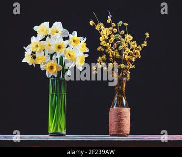Ein Bouquet von Narzissen und ein Bouquet von Blüten weiden- und Hundezweige mit gelben Blüten in Glasvasen Auf einem Holztisch auf einem schwarzen b Stockfoto