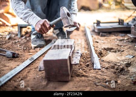 Nahaufnahme Hände eines Schmieds trifft Eisen oder Stahlblech mit einem Hammer in einer Werkstatt im Freien. Stockfoto