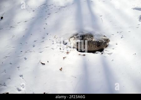 Metallabdeckung eines Kanals oder Abflusses, zwischen den Schneeverwehungen, an einem sonnigen Tag. Stockfoto
