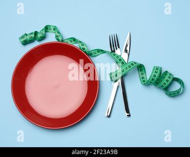 Rote runde Platte und Gabel und Messer in grün eingewickelt Maßband auf blauem Hintergrund Stockfoto