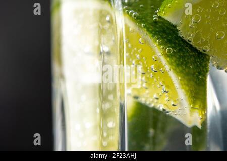 Limettenscheibe mit Tropfen in kohlensäurehaltiges Mineralwasser. Sommerdrink-Konzept. Stockfoto