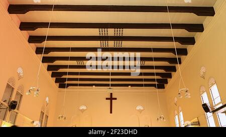 Wand hinter dem Altar: Kreuz an der Wand, hängende Lichter und horizontale Holzbalken an der Wand der Christ Church in Malacca (Melaka) Malaysia Stockfoto