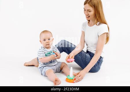 Mama und ihr Baby spielen mit bunten Regenbogen Pyramide Spielzeug, auf einem isolierten weißen Hintergrund, Spielzeug für kleine Kinder, Kind mit Lernspielzeug, früh Stockfoto