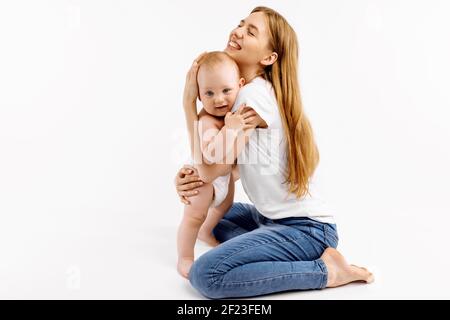 Portrait der jungen Mutter und ihrem einjährigen Sohn, liebevolle Mutter umarmt und küsst ihr Baby auf isoliertem weißem Hintergrund Stockfoto