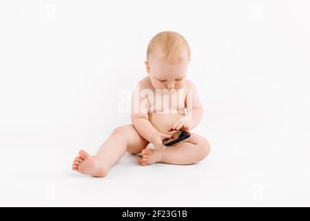 Kleines Baby in einer Windel, mit einem Handy sitzt auf einem isolierten weißen Hintergrund Stockfoto