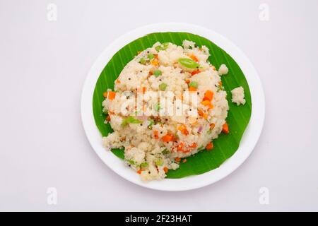 UPMA aus Samolina oder rava Upma, dem berühmtesten südindischen Frühstückselement, das in einem Teller mit frischem Bananenblatt auf whit gelegt angeordnet ist Stockfoto