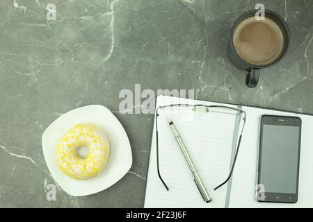 Runder Donut in Schokolade auf einem weißen Teller. Donut mit weißer Schokolade bedeckt und mit Zitronenschale bestreut. Donut und Kaffee auf dem Tisch. Platz für Stockfoto