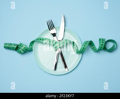 Grüne runde Platte und Gabel und Messer in grün eingewickelt Maßband auf blauem Hintergrund Stockfoto