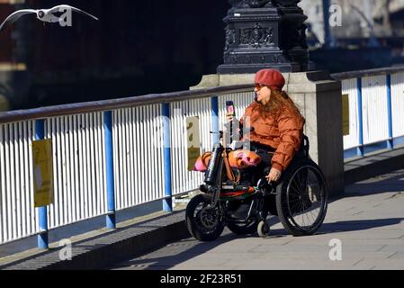 London, England, Großbritannien. Frau im Rollstuhl, die ein Foto auf ihrem Mobiltelefon auf der South Bank gemacht hat Stockfoto