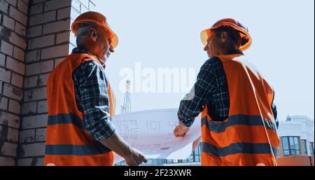 Low-Angle-Ansicht von Bauherren in Sicherheitswesten mit Blaupause Gespräche auf der Baustelle Stockfoto