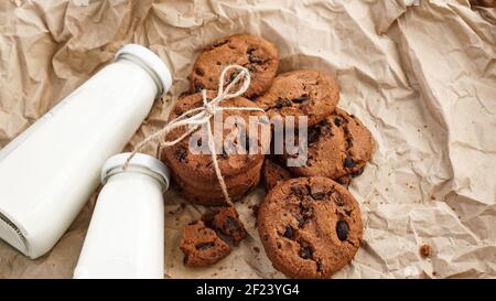 Kekse mit Schokoladentropfen auf Bastelpapier und Flaschen Milch Stockfoto