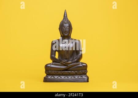 Kleine Bronze Thai buddha Statue vor einem gelben nahtlosen Hintergrund In meditativer Haltung Stockfoto