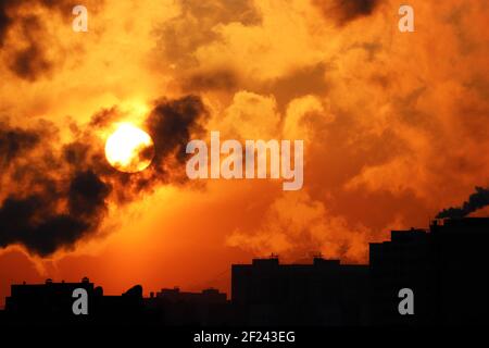 Sonnenaufgang am bunten dramatischen Himmel, orange Sonne scheint durch dunkle Wolken über den Gebäuden Silhouetten. Malerische Stadtlandschaft für Horror Stockfoto