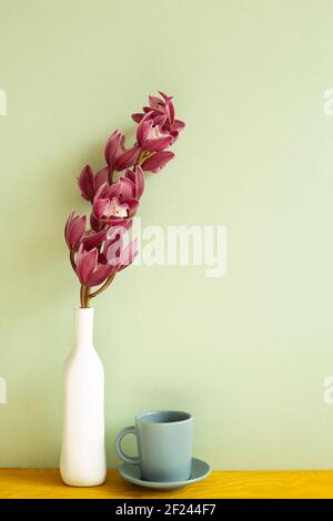 Kaffeetasse und Vase aus Cymbidium Blumen auf Holztisch. Grüner Hintergrund Stockfoto