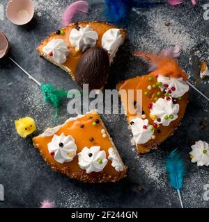 Blick aus der Vogelsicht auf einige Stücke von mona de pascua, einem Kuchen, der am Ostermontag in Spanien gegessen wurde, geschmückt mit einem Plüschküken, einem Schokoladenei und Federn Stockfoto