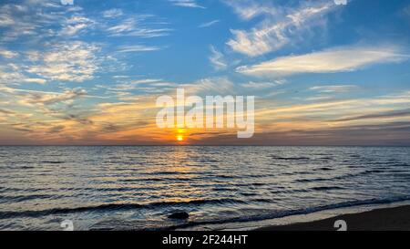 Schöner Sonnenuntergang am Meer mit orangefarbenem Licht und goldenem Glanz im Wasser mit blauem Himmel. Sie können schöne goldene Cumulus Wolken sehen. Meerwasser f Stockfoto