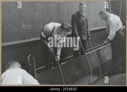 Evacuatie via de Nachtwachtleuf im Jahr 1939; Evacuatie van het Rijksmuseum vanwege oorlogsdreiging, augustus - november 1939.Männer lassen einen Malkasten durch den Nachtwachschlitz im Boden des Ehrenraumes, der direkt zur Unterführung führt. Im Jahr 1939 fand die Evakuierung vieler Fälle im Zusammenhang mit der Kriegsgefahr statt. Das Museum wurde geschlossen. Stockfoto
