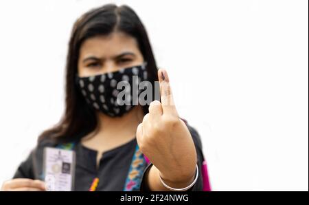 Selektiver Fokus auf den mit Tinte markierten Finger einer Inderin mit Sicherheits-Gesichtsmaske und Wählerkarte auf der anderen Seite Stockfoto