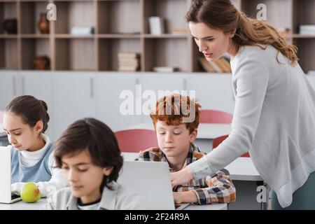 Lehrer hilft Schuljunge mit Laptop im Klassenzimmer, verschwommen Vordergrund Stockfoto