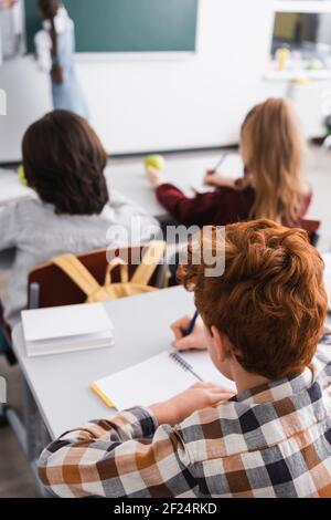 Rückansicht von Schülern, die in Notizbüchern im Klassenzimmer schreiben, verschwommener Hintergrund Stockfoto