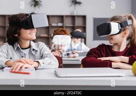 Glückliche Klassenkameraden, die einander beim Spielen in vr Headsets im Klassenzimmer Stockfoto