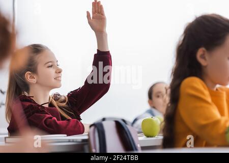 Lächelndes Schulkind, das die Hand neben Apfel hebt und im Klassenzimmer bucht Stockfoto