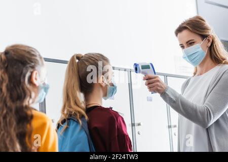 Lehrer in Schutzmaske mit Infrarot-Thermometer auf Schülerinnen während Quarantäne in der Schule Stockfoto
